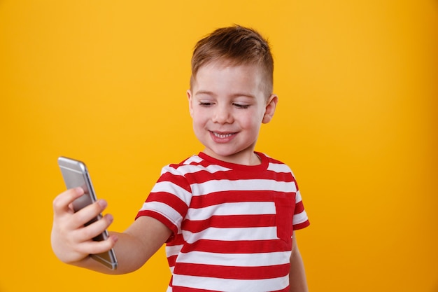 Foto gratuita niño pequeño sonriente que sostiene el teléfono móvil y que hace selfie