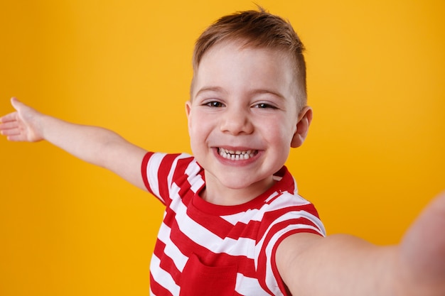 Foto gratuita niño pequeño sonriente que sostiene el teléfono móvil y que hace selfie