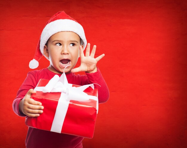 Niño pequeño sorprendido con gorro de santa claus y un regalo