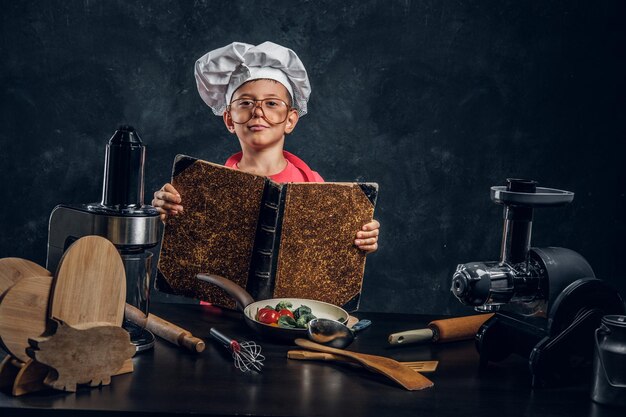 El niño pequeño tiene una gran idea sobre la cocina: está leyendo un libro de recetas.