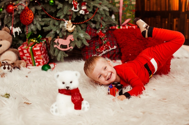 Niño pequeño en traje rojo festivo juega antes de un árbol de Navidad