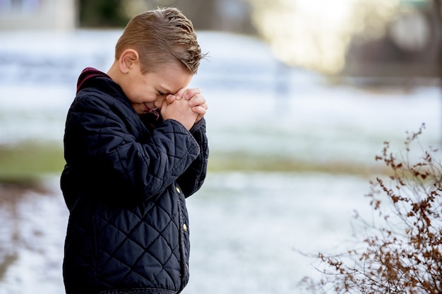 Niño de pie con los ojos cerrados y rezando