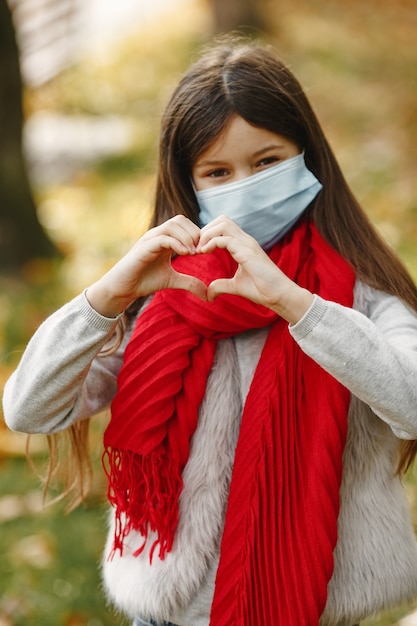 Foto gratuita niño de pie en el parque otoño. tema de coronavirus. chica con un pañuelo rojo.