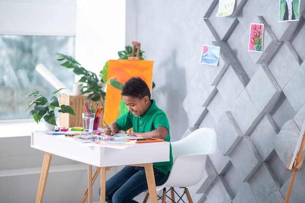 Niño de piel oscura dibujando en la mesa en la sala de luz