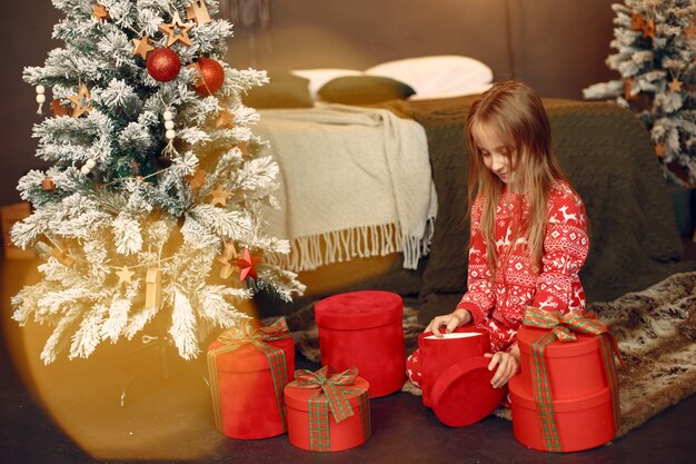 Niño en pijama rojo. Hija sentada cerca del árbol de Navidad.