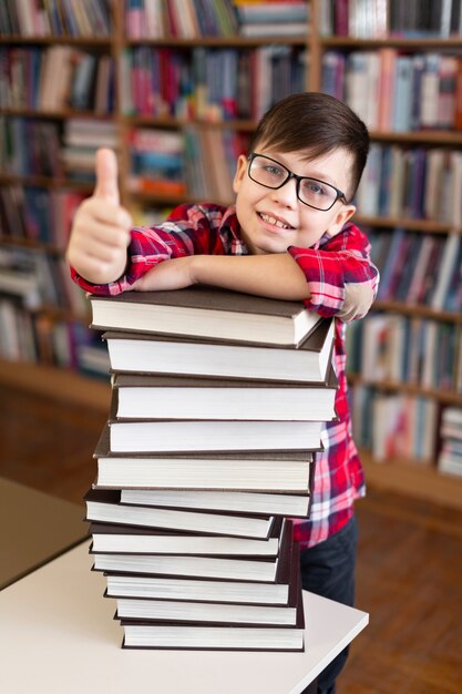 Niño con pila de libros que muestra signo ok