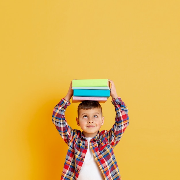 Foto gratuita niño con pila de libros sobre su cabeza.