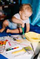 Foto gratuita niño con pincel pintando sobre papel cerca de acuarelas y sentado en una colcha