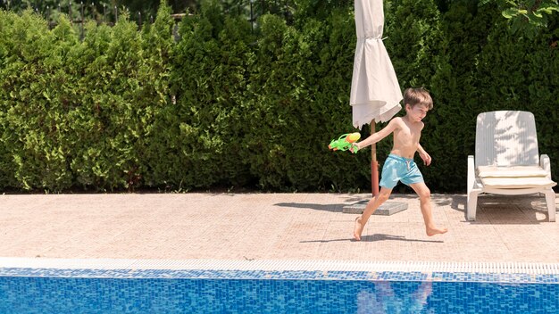 Niño en la piscina jugando con pistola de agua