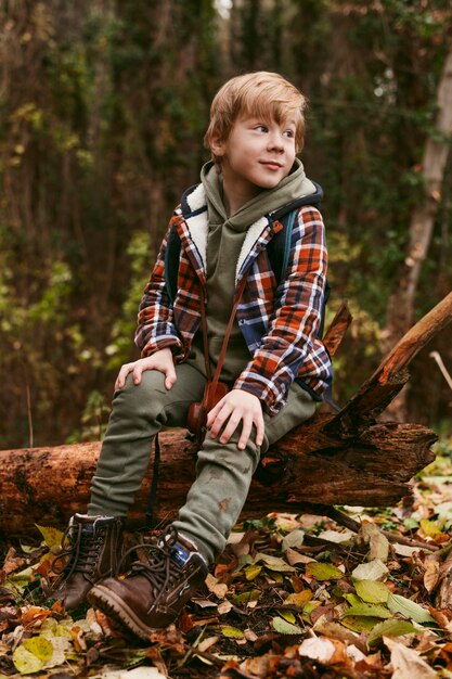 Niño posando en la naturaleza sentado en el tronco de un árbol
