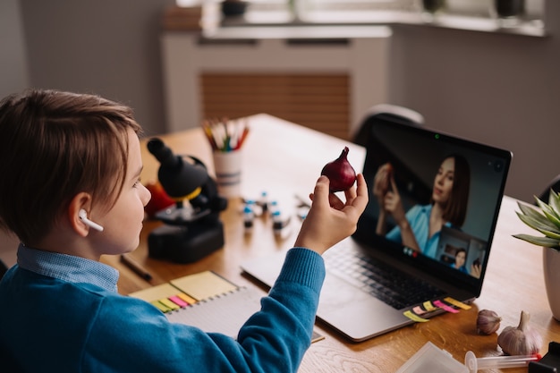 Un niño preadolescente usa una computadora portátil para hacer una videollamada con su maestra