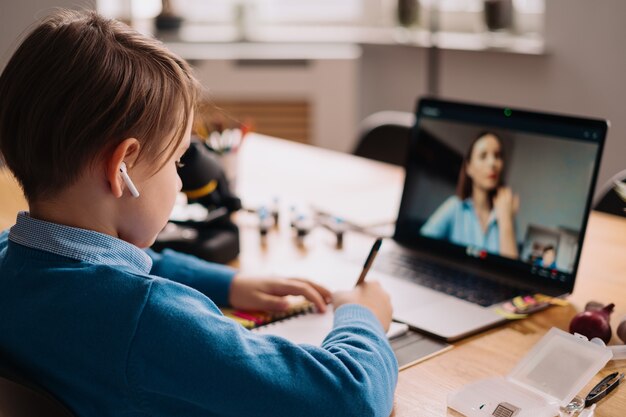 Un niño preadolescente usa una computadora portátil para hacer una videollamada con su maestra