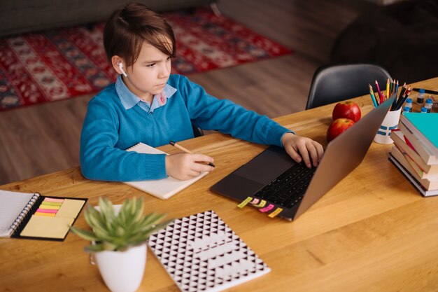 Un niño preadolescente usa una computadora portátil para hacer una videollamada con su maestro, clases en línea, tomar notas