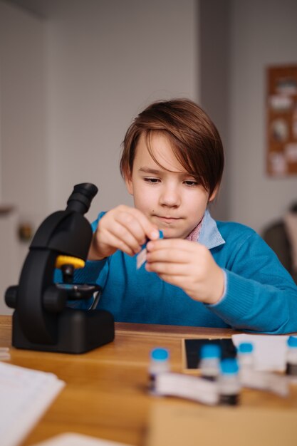 Niño de primer grado estudiando en casa usando microscopio