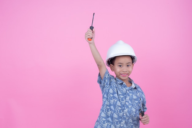 Foto gratuita un niño que hizo un gesto con las manos y llevaba un casco sobre un fondo rosa.