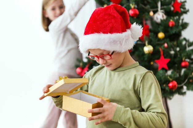 Foto gratuita niño con un regalo dorado y un sombrero de papa noel