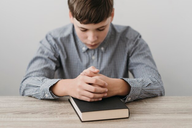 Niño rezando con las manos sobre una Biblia