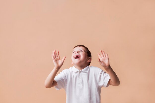 Niño riendo mirando hacia arriba con la mano gesticulando sobre fondo beige