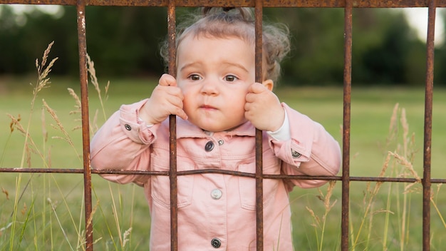 Niño en ropa rosa detrás de las rejas del parque tiro medio