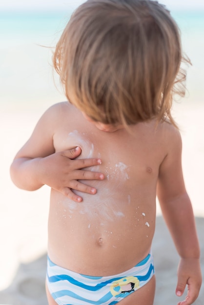 Niño rubio en la playa mirando hacia abajo tiro medio