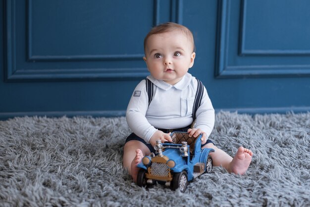 Niño rubio sentado en una alfombra y jugando con un coche azul.