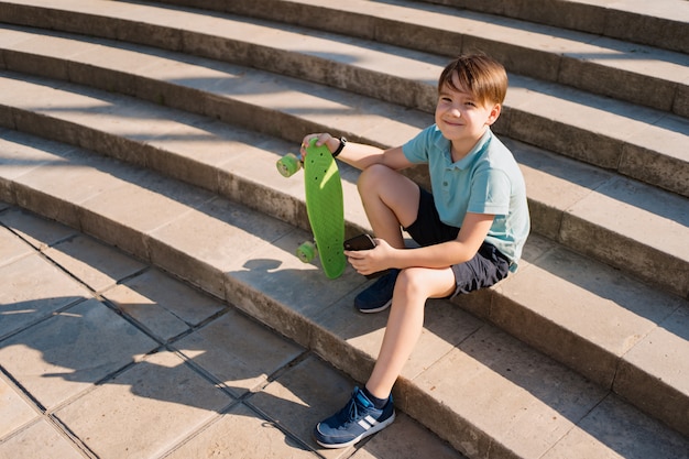 Niño sentado en las escaleras con el teléfono inteligente en la mano y penique verde viendo videos graciosos