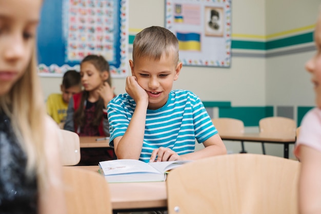 Niño, sentado, escuela, escritorio, lectura, libro