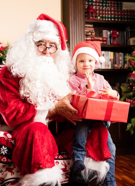 Niño sentado en las piernas de papa noel con un regalo