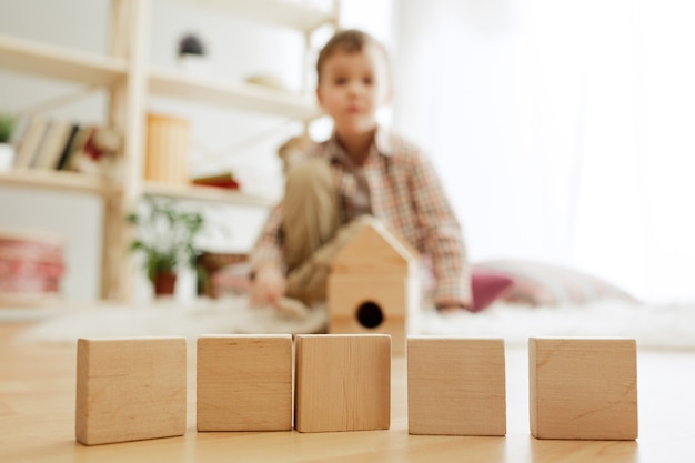 Foto gratuita niño sentado en el suelo. chico guapo jugando con cubos de madera en casa.