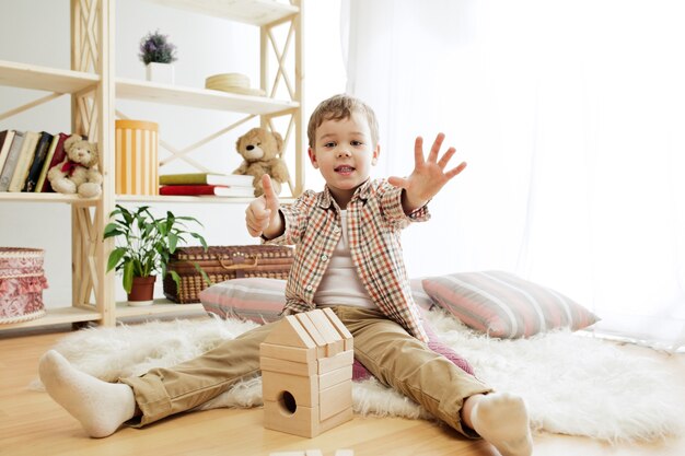 Niño sentado en el suelo. Chico guapo jugando con cubos de madera en casa.