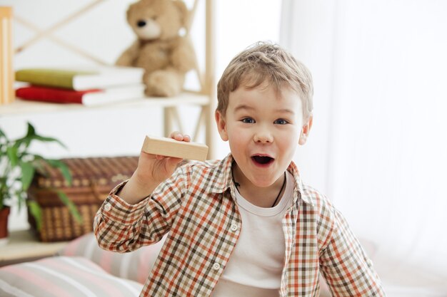 Niño sentado en el suelo. Muchacho sorprendido muy sonriente que juega con cubos de madera en casa. Imagen conceptual con copia o espacio negativo.