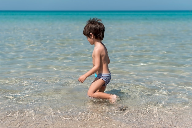 Niño de Sideview en la playa jugando en el agua