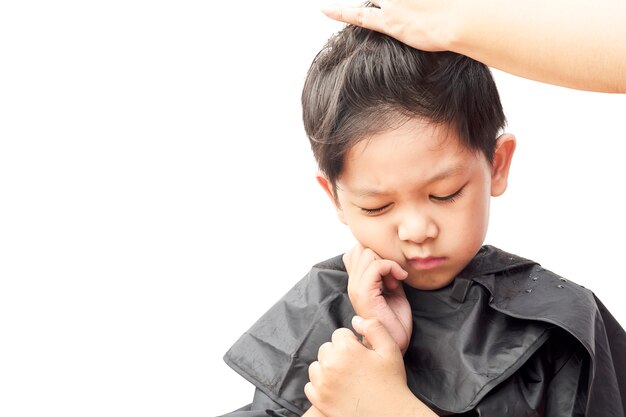 Un niño siente picazón mientras se corta el cabello peinadora aislada sobre fondo blanco