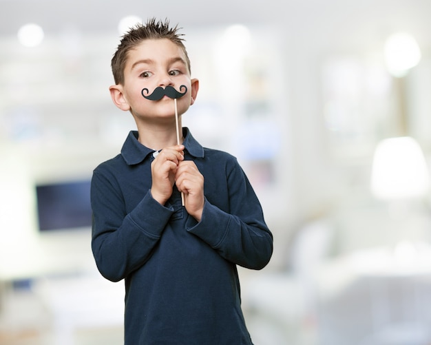 Niño simpático posando con un bigote falso