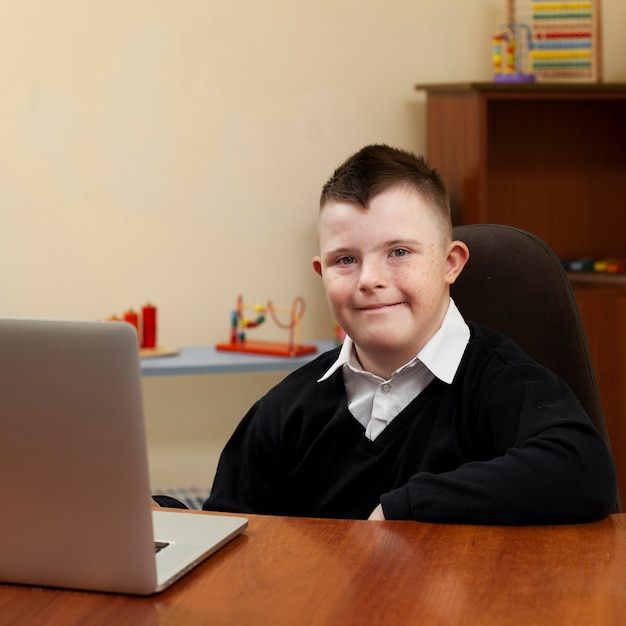 Foto gratuita niño con síndrome de down posando con laptop