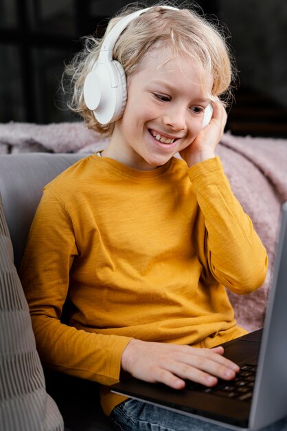 Niño, en, sofá, con, computadora portátil, y, auriculares