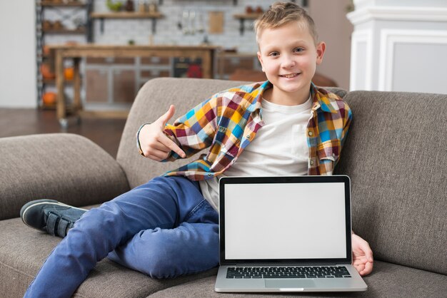 Niño en sofá enseñando pantalla de portátil