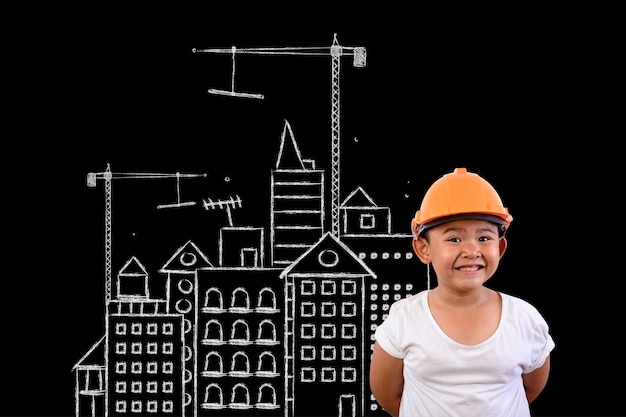 Foto gratuita un niño con un sombrero de ingeniero y un plan de casa en una pizarra