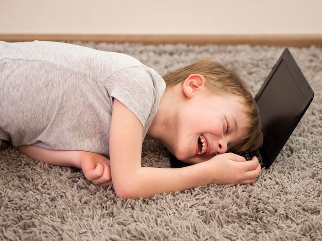 Niño sonriente acostado con la cabeza en una computadora portátil