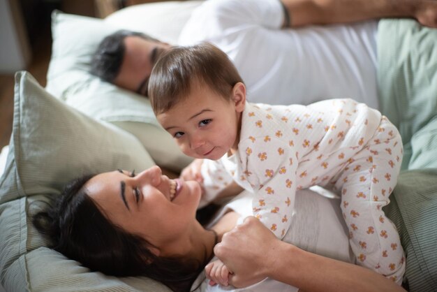 Niño sonriente acostado en la cama con su mamá en la mañana