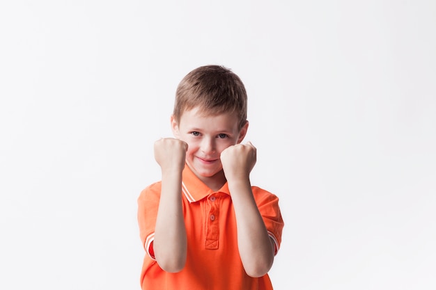 Foto gratuita niño sonriente apretando el puño haciendo sí gesto en la pared blanca mirando a la cámara