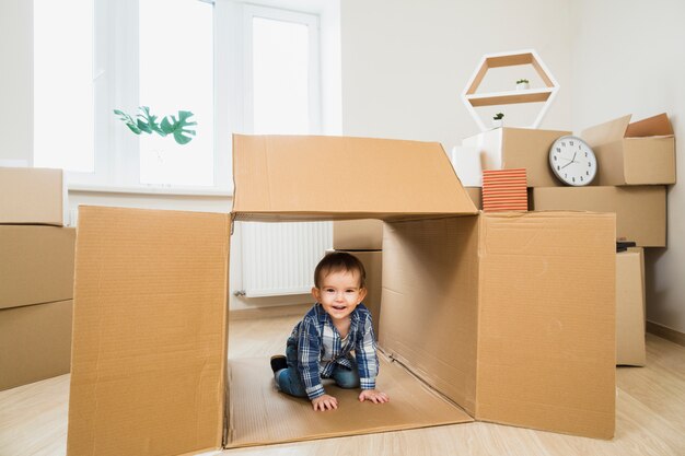 Niño sonriente del bebé dentro de una caja de cartón abierta en casa