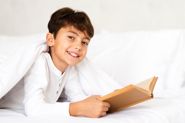 Niño sonriente cubierto con una manta mientras lee
