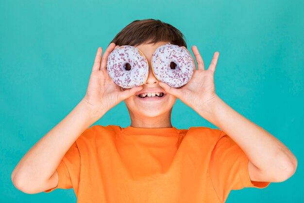 Niño sonriente cubriéndose los ojos con donas