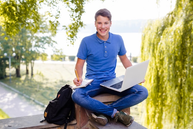 Niño sonriente estudiando con la computadora portátil en el parque