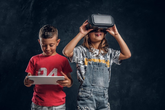 Un niño sonriente feliz sostiene una tableta mientras una chica graciosa lleva gafas vr.