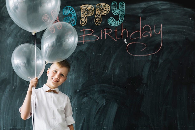 Niño sonriente con globos cerca de la escritura del feliz cumpleaños