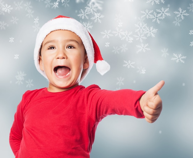 Niño sonriente con gorro de santa y un gesto positivo