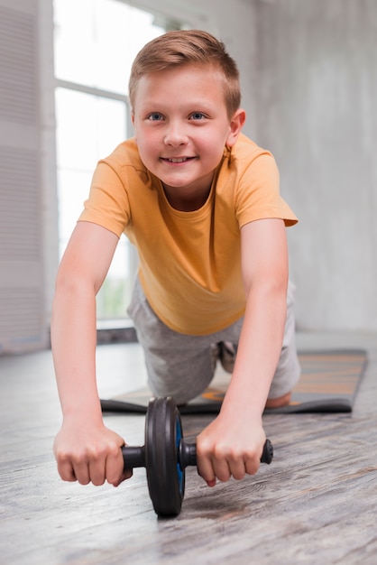 Niño sonriente haciendo ejercicio de lanzamiento de rueda ab en piso de madera dura