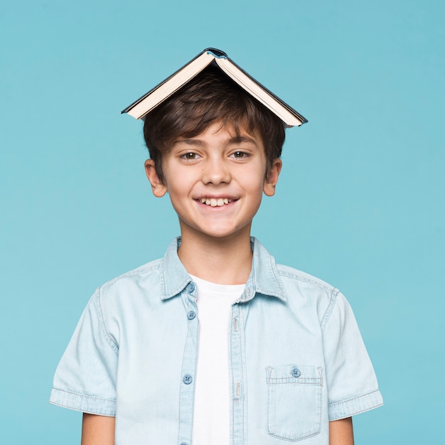 Foto gratuita niño sonriente con libro en cabeza